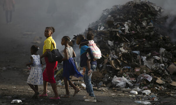 28일(현지시간) 한 여자와 아이들이 연기가 나는 쓰레기 더미 옆으로 걸어가고 있다. 포르토프랭스=AP연합뉴스
