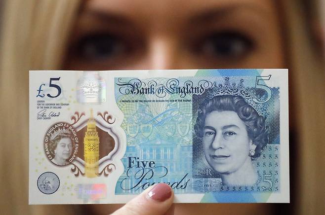 한 여성이 엘리자베스 2세 여왕의 이미지가 들어간 5파운드 지폐를 들어보이고 있다.