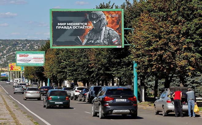 20일(현지 시각) 러시아군이 점령한 우크라이나 동부 루한스크 거리에서 차들이 친러시아 구호가 적힌 옥외 광고판을 지나가고 있다.