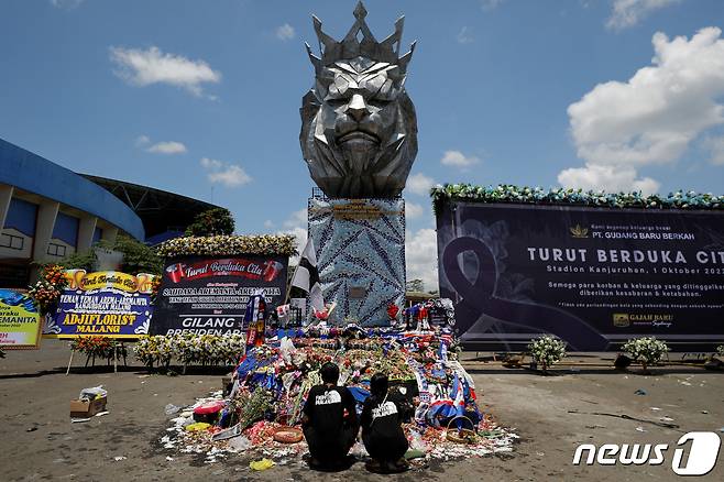 축구장 참사가 벌어졌던 인도네시아 자바주(州) 말랑의 축구 경기장에서 4일(현지시간) 아르마FC 축구 팬 두 명이 조화가 쌓인 구단 동상 앞에 앉아 애도하고 있다.. ⓒ 로이터=뉴스1 ⓒ News1 김성식 기자