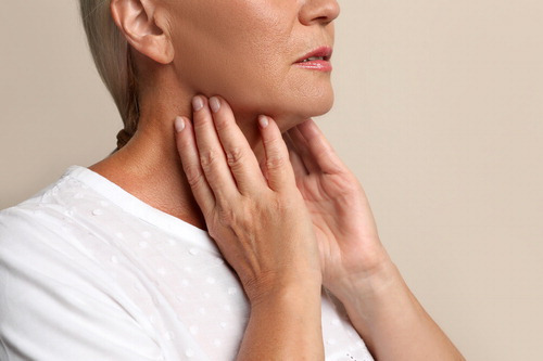 Mature woman doing thyroid self examination on beige background closeup