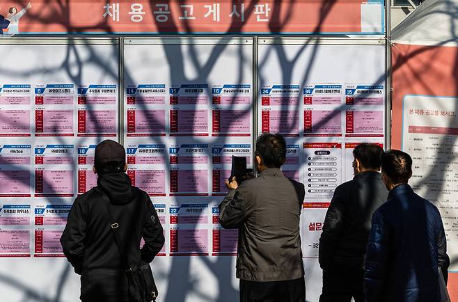 16일 오후 서울 강동구 강동구청에서 열린 2022 강동 취업박람회에서 구직자들이 앙상한 나무 그림자가 비친 채용공고 게시판을 꼼꼼하게 읽고 있다. [사진출처 = 연합뉴스]