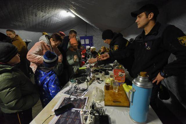 24일 러시아군의 공격으로 우크라이나 키이우 일대에 대규모 정전이 발생하자 보호소에 모인 시민들이 몸을 녹이며 휴대전화를 충전하고 있다. 키이우=EPA 연합뉴스