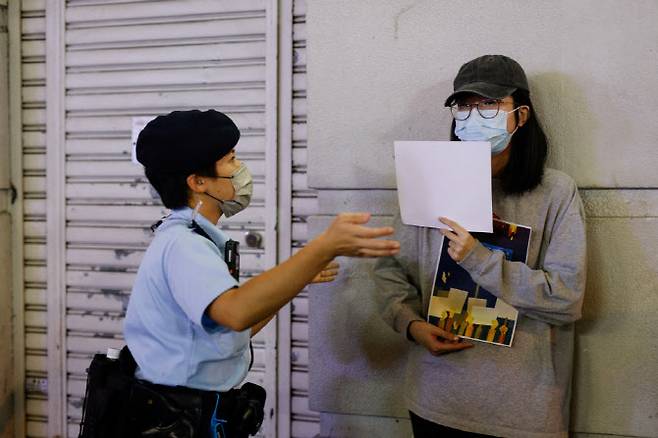28일(현지 시각) 중국 우루무치 화재 희생자 추모 행사에서 한 경찰관이 당국의 봉쇄 정책에 항의하기 위해 흰색 종이를 들고 있는 여성에게 나가달라고 요청하고 있다. (사진=연합뉴스)