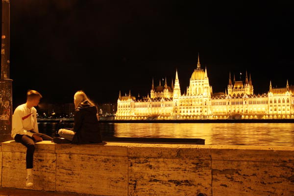 헝가리 부다페스트에서 젊은 연인들이 다뉴브 강변 벤치에 앉아 국회의사당 야경을 보고 있다.