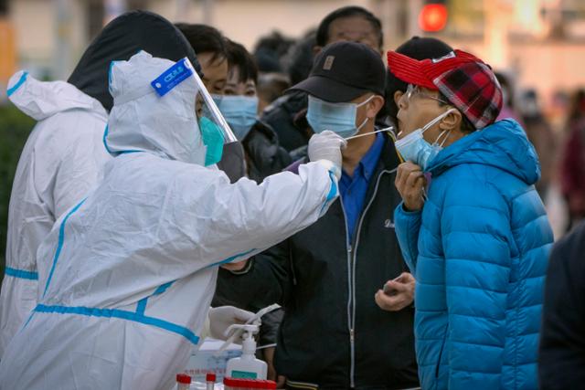 중국 베이징의 코로나19 검사장에서 방호복을 입은 의료진이 시민들의 입에서 검체를 채취하고 있다. 베이징=AP 연합뉴스