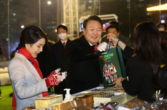 윤석열 대통령과 김건희 여사가 지난 16일 오후 서울 종로구 열린송현광장에서 열린 윈·윈터 페스티벌 개막식에서 에어돔 부스를 방문, 물건을 구입하고 있다. 연합뉴스