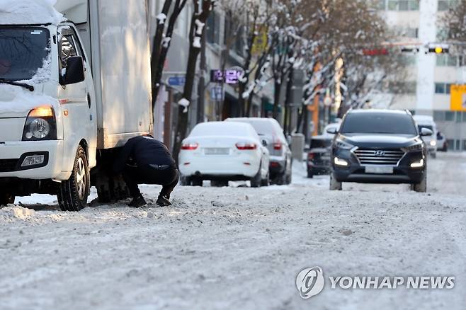 눈 덮인 도심 이면도로 (광주=연합뉴스) 정회성 기자 = 19일 오전 광주 서구 상무1동 주택가에서 화물차 운전기사가 바퀴에 체인을 감고 있다. 2022.12.19 hs@yna.co.kr