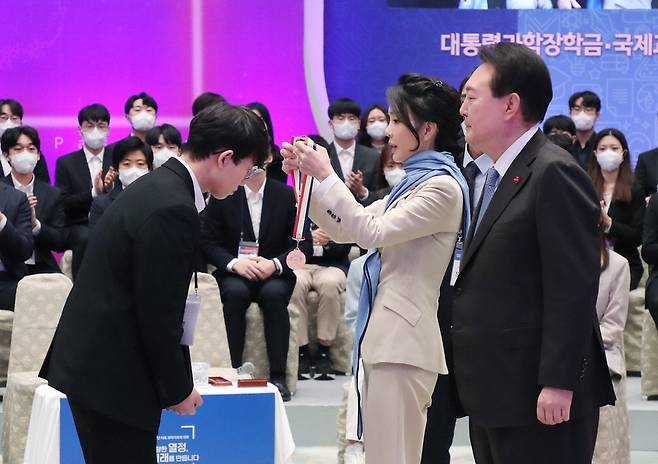 윤석열 대통령의 부인 김건희 여사(가운데)가 22일 청와대 영빈관에서 열린 '미래 과학자와의 대화'에서 윤 대통령이 지켜보는 가운데 대통령과학장학생·국제과학올림피아드 수상자에게 메달을 걸어주고 있다.  <이승환 기자>