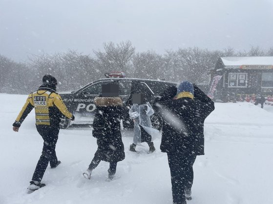 매서운 강풍과 함께 많은 눈이 내리는 22일 한라산 1100고지 휴게소에 설경을 보러 갔던 관광객들이 고립돼 제주도 자치경찰단이 구조하고 있다. 연합뉴스