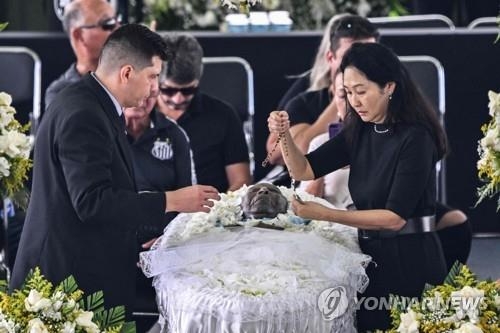 축구황제 펠레의 부인 마르시아 아오키(오른쪽)가 2일(현지시간) 산투스 빌라 베우미루 경기장에 안치된 펠레의 관 위에 묵주를 놓고 있다. [산투스=AFP/연합뉴스]