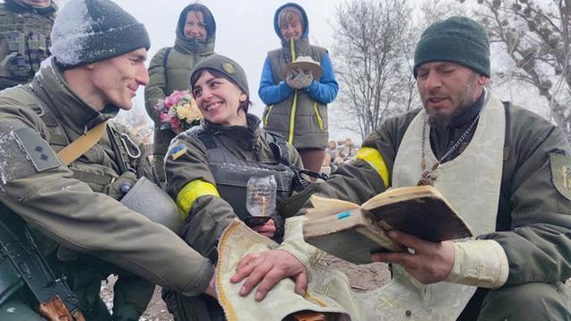 지난해 3월 8일 우크라이나 방위군 올렉산드르(왼쪽)와 올레나(가운데)가 미상의 검문소에서 정교회 사제가 주관한 가운데 열린 결혼식에서 서로를 바라보고 있다. 우크라이나=로이터 연합뉴스