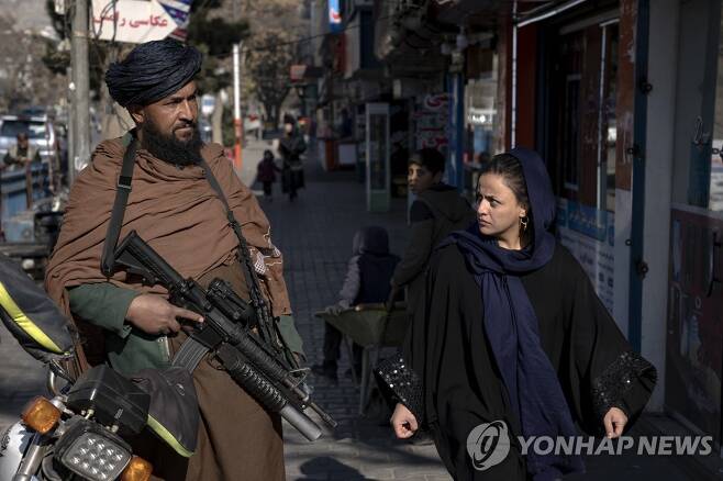 카불에서 경비를 서는 탈레반 전사 옆을 지나가는 여성 [AP 연합뉴스 자료사진. 재판매 및 DB 금지]