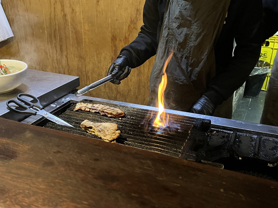 An employee grills pork belly before serving it with the meat noodles. [LEE TAE-HEE]