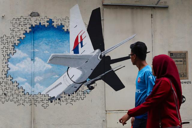 2014년 승객과 승무원 239명을 태우고 말레이시아 쿠알라룸푸르에서 중국 베이징을 향하던 중 인도양에서 사라진 말레이항공 MH370편 실종 5주기를 하루 앞둔 2019년 3월 쿠알라룸푸르 외곽 샤 알람에서 한 커플이 추모 벽화 앞을 지나가고 있다. 쿠알라룸푸르=EPA 연합뉴스