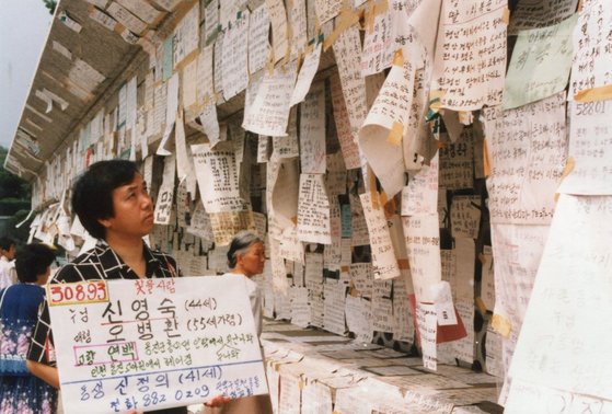 KBS '이산가족을 찾습니다' 당시 신청 번호를 쓴 피켓을 든 이산가족이 벽보를 유심히 살펴보고 있다. 사진 국가기록원 나라기록관