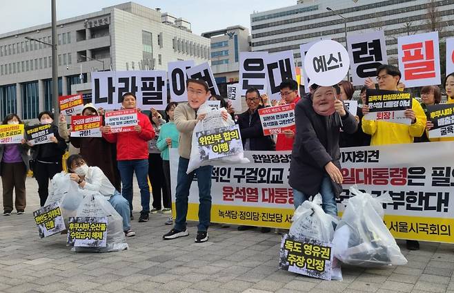 17일 서울 용산구 전쟁기념관 앞에서 열린 서울시국회의 기자회견을 마친 뒤 기시다 후미오 일본 총리 가면을 쓴 사람이 '위안부 합의이행', '독도 영유권 주장 인정', '한반도 자위대 진출' 등이 적힌 쓰레기봉투를 윤석열 대통령 가면을 쓴 이에게 건네는 퍼포먼스를 하고 있다. ⓒ연합뉴스