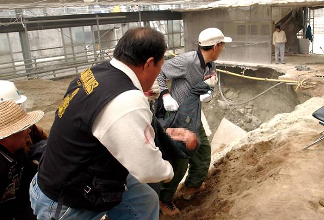 2002년 4월9일 경기도 이천시 대월면 협업농장 아가동산 사체 발굴 현장. 발굴 도중 유리온실 바닥 콘크리트가 무너지면서 작업 인부가 함께 추락해 부상을 당하자 다른 인부들이 부상자를 병원으로 옮기고 있다. 부상자는 1988년 숨져 아가동산에 묻힌 것으로 알려진 강민경씨(당시 21세)의 아버지 강성진씨다. ⓒ연합뉴스