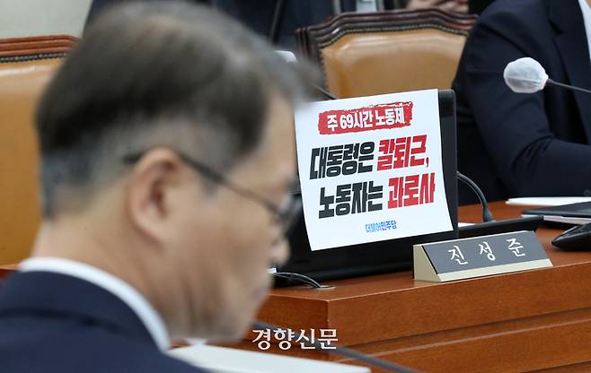 이정식 고용노동부장관이 21일 국회 환경노동위 전체회의에서 민주당 의원들이 부착한 ‘대통령은 칼퇴근 노동자는 과로사’라고 적힌 피켓 앞에서 심각한 표정으로 질문을 듣고 있다. 박민규 선임기자