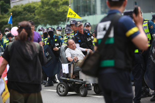 전동 휠체어 스쿠터를 타고 차도 시위에 나선 이규식을 경찰들이 둘러싸서 막고 있다. 이규식은 중증 뇌병변 장애인이자 지난 20여년간 한국 장애인 운동의 최일선에 서 있었다. 최인기 제공