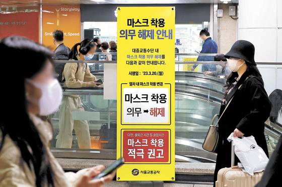 People pass by a notice at a subway station in Seoul that informs of the mask mandate lift in public transportation on March 19, a day before the change. [JOONGANG ILBO]
