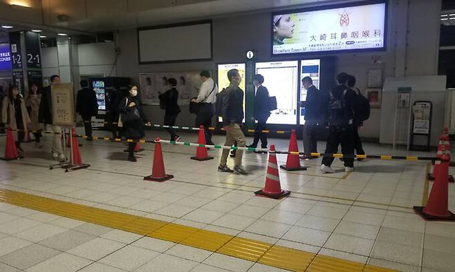 일본 도쿄 오사키역에서 지난 4월 24일 퇴근하는 시민들이 가로 분리봉을 따라 한 줄로 플랫폼으로 향하고 있다. 이 역에서는 승객이 한꺼번에 몰려 병목 현상이 벌어지는 것을 막기 위해 퇴근 시간대에는 가로 분리봉을 설치해 시민 이동을 유도하고 있다. 도쿄=강구열 특파원