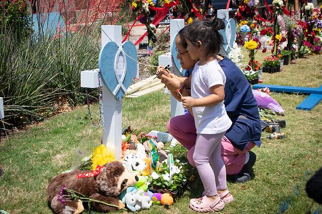 총기 난사 사건이 일어난 미국 텍사스주 댈러스 교외 앨런의 쇼핑몰 앞에서 8일(현지시각) 한 여성과 아이가 희생자들을 추모하는 팻말에 글을 적고 있다. 연합뉴스