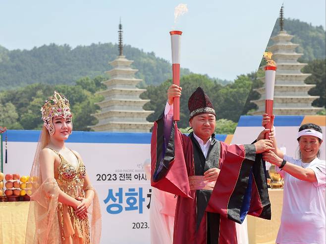 11일 오전 김관영 전북도지사(대회 조직위원장)가 익산 미륵사지에서 주선녀에게 채화된 성화를 전달 받은 후(사진 왼쪽) 대회 참가자 김영순씨에게 넘겨주고 있다. 전라북도 제공