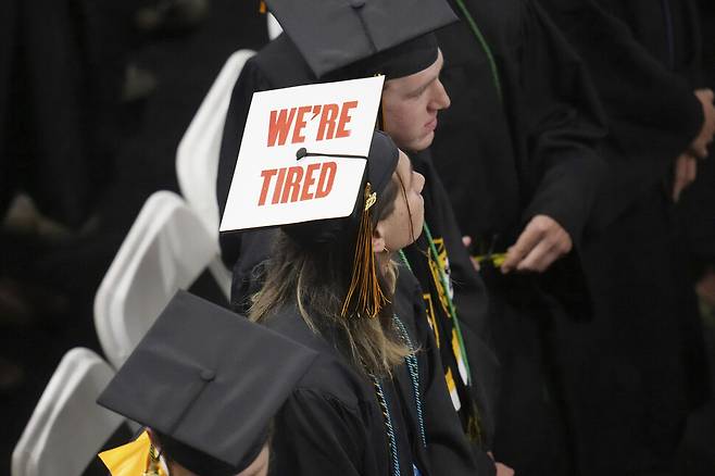 한 학생이 “우리는 지쳤다”라는 피켓을 졸업 모자에 붙인 채 등을 돌려 앉아있다. AP 연합뉴스