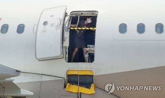 지난 26일 오후 제주공항에서 출발해 대구공항에 비상구 출입문이 열린 채 착륙한 아시아나항공기에서 한 승무원이 문에 안전바를 설치한 뒤 두 팔을 벌려 막고 있다. [대구국제공항 관계자 제공]