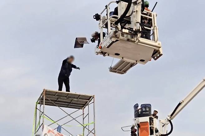 31일 오전 전남 광양시 금호동 포스코 광양제철소 인근 도로에서 높이 7ｍ 망루를 설치해 고공농성을 벌인 한국노총 금속노련 간부가 체포에 나선 경찰관에게 의자를 던지며 저항하고 있다. [연합]