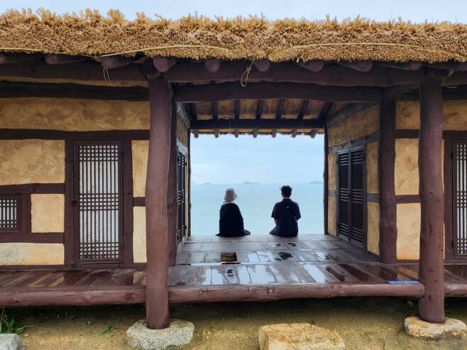 여행자들이 액자 프레임 같은 자산어보 촬영지 마루에 앉아 바다를 보고 있다.