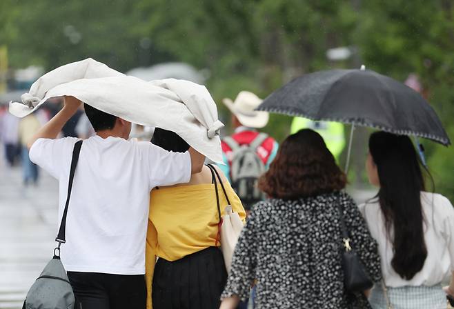 광화문광장을 지나는 시민들이 지난 6일 갑자기 쏟아지는 비를 옷으로 막으며 걸어가고 있다. 연합뉴스