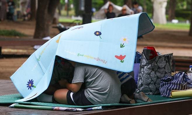 소나기가 내린 지난 6일 서울 성동구 서울숲에서 휴식하던 한 가족이 갑자기 내린 비에 돗자리를 우산 삼아 쓰고 있다. 연합뉴스