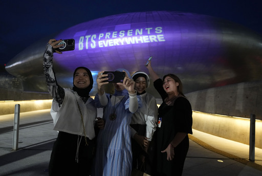 The landmark Dongdaemun Design Plaza is illuminated in purple as fans take a selfie in Seoul, South Korea, Monday, June 12, 2023. AP