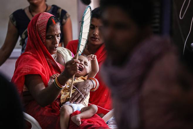 2022년 5월 21일 인도 우타르프라데시주 미르자푸르의 지역 병원에서 한 여성이 폭염으로 인해 비위생적인 물을 마셔 병에 걸린 어린이에게 부채질을 해 주고 있다.
