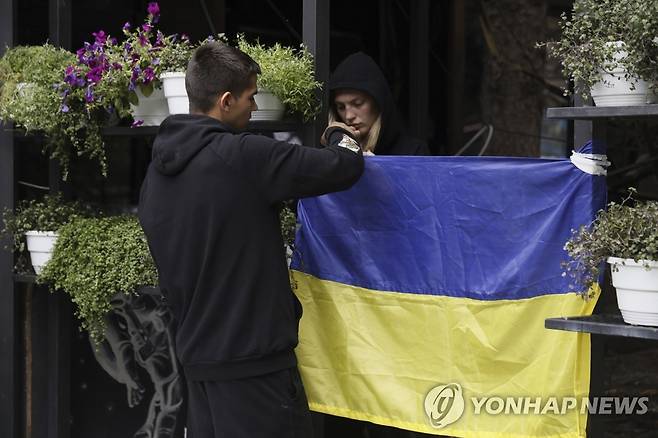 사람들이 도네츠크 지역에서 러시아 공격을 받은 식당 입구에 우크라이나 국기를 걸고 있다. [AP=연합뉴스]