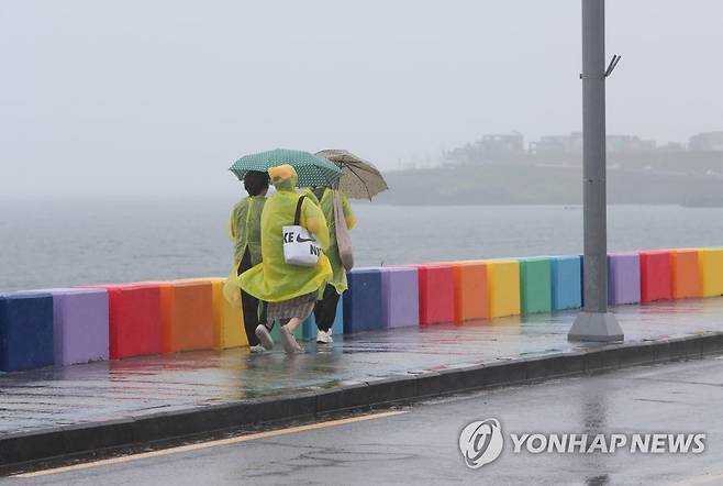 장맛비 내리는 제주 [연합뉴스 자료사진] 제주도가 장마철에 접어든 지난 6월 제주시 도두동 무지개 해안도로에서 관광객들이 비옷을 입고 우산을 쓴 채 길을 걷고 있다.