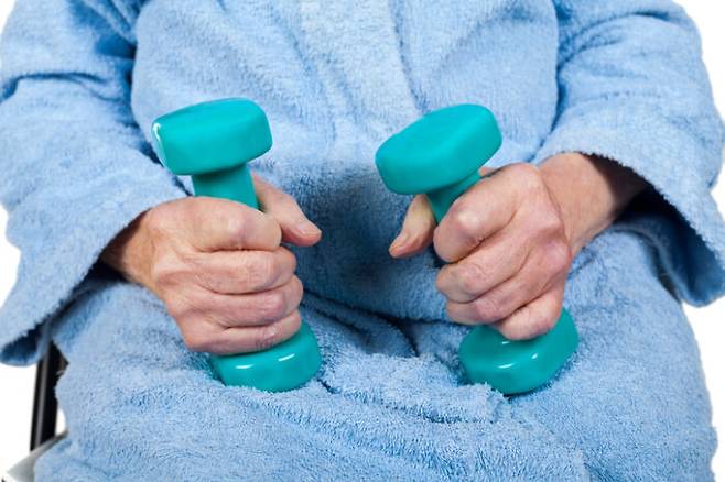 Close up picture of senior woman's hands holding blue dumbells, physiotherapy on isolated