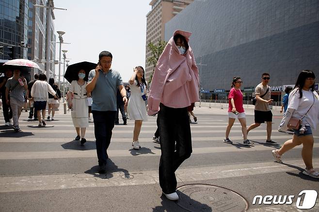 16일 중국 베이징에서 폭염 경보가 발령된 가운데 한 시민이 햇빛을 가리기 위해 옷으로 상체를 덮은 채 이동하고 있다. 2023.06.16 ⓒ 로이터=뉴스1 ⓒ News1 최종일 기자