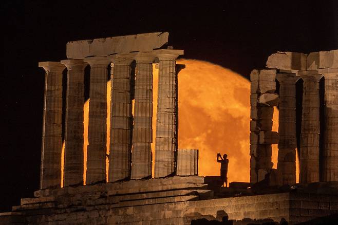 2023년 7월 3일 그리스 아테네 인근 수니온 곶에 있는 포세이돈 신전 뒤로 '벅 문'으로 알려진 보름달이 떠오르는 가운데 한 사람이 사진을 찍고 있다. /로이터 뉴스1