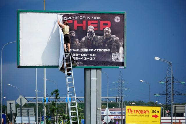 지난달 24일 러시아 상트페테르부르크의 고속도로에서 한 남성이 '바그너그룹에 들어오라'라고 쓰인 포스터를 떼고 있다. 상트페테르부르크=AP 뉴시스