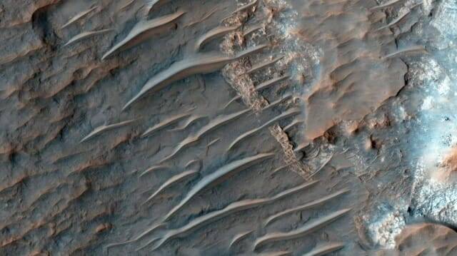 암석 표면을 가로질러 흐르는 적갈색 사구를 보여주는 사진. NASA MRO 탐사선이 촬영한 화성 모래언덕의 TAR의 모습 (이미지 제공: NASA/JPL–칼텍/애리조나대학)