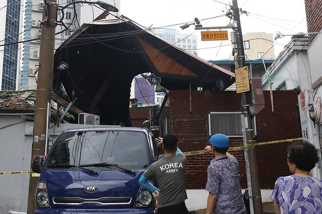 11일 오후 대구 도심에 기습적인 폭우가 쏟아진 가운데 중구 남산동의 한 주택 지붕이 크게 파손된 채 옆집에 걸쳐 있는 모습을 주민들이 바라보고 있다. /뉴스1