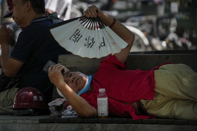 16일(현지시간) 중국 베이징에서 한 남성이 무더운 날 벤치에서 스마트폰을 보며 선풍기로 몸을 식히고 있다. AP연합뉴스