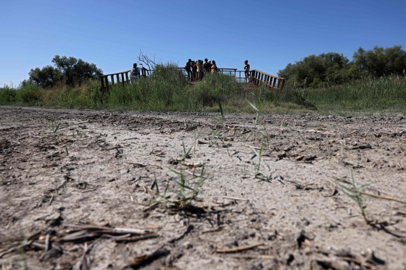 SPAIN-POLITICS-ELECTIONS-ENVIRONMENT-DROUGHT - People stand on an abandoned boat jetty where a river once flowed, due to low rainfall and intensive irrigation of farmland at the Tablas de Daimiel, in the Castilla La Mancha region, on July 13, 2023. The water management divides political parties ahead of July 23 general elections, as Spain is grappling with a severe drought and successive heatwaves that has put the country at the forefront of the climate crisis in Europe. (Photo by Thomas COEX / AFP)