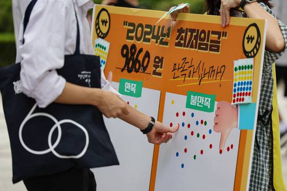 People vote on whether they agree with the decided minimum wage for next year in central Seoul on Wednesday. The right side shows they are dissatisfied. [YONHAP]