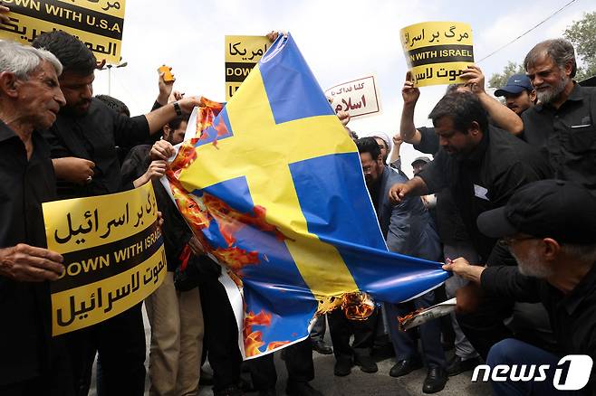 이란 시위대가 지난 21일(현지시간) 수도 테헤란에서 최근 스웨덴에서 벌어진 쿠란 소각시위에 항의하는 차원에서 스웨덴 국기에 불을 지르고 있다. 2023.7.21. ⓒ 로이터=뉴스1 ⓒ News1 김성식 기자
