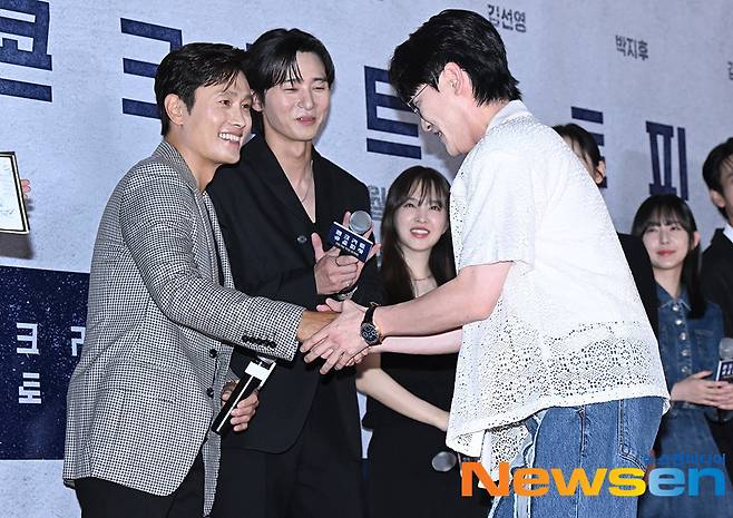 Actor Lee Byung-hun, left, and singer Young-tak shake hands at a VIP Test screening photo wall for the movie Concrete Utopia at Lotte Cinema World Tower in Songpa-gu, Seoul, in the afternoon of August 8.