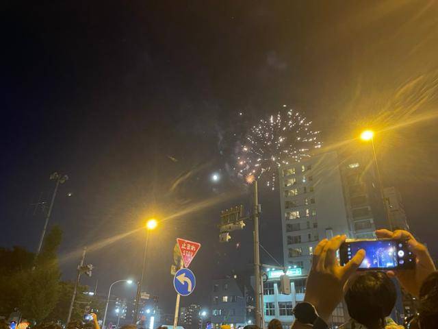 지난 7월 29일 일본 도쿄 스미다강에서 펼쳐진 4년 만의 불꽃놀이 때 한 시민이 빌딩 사이로 살짝 보이는 불꽃을 스마트폰으로 촬영하고 있다. 이날 유료석을 구매하지 못한 대부분의 사람들은 인파에 밀려 제대로 관람할 수 있는 자리를 찾지 못했다. 도쿄=최진주 특파원